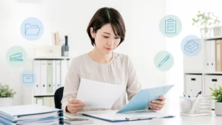 備品台帳と書類を確認する中小企業の総務担当者